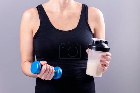 woman holds a glass of collagen in one hand and a dumbbell in the other. Sports nutrition: drink with proteins