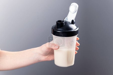 A female hand holds a mixer glass with collagen on a gray background. Sports nutrition: drink with proteins.