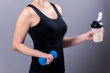 woman holds a glass of collagen in one hand and a dumbbell in the other. Sports nutrition: drink with proteins