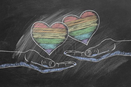 Foto de Dos manos masculinas con corazones de arco iris. Derechos LGBT, LGBTQIA y concepto de igualdad de género. El mes del orgullo. Declaración de amor, aceptación de sentimientos, dar amor. - Imagen libre de derechos