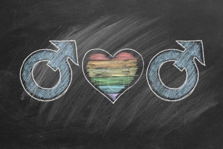 Foto de Símbolos de género para hombres interconectados con un corazón con colores de arco iris dibujados en una pizarra. Concepto LGBT - Imagen libre de derechos