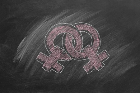 Téléchargez les photos : Deux symboles féminins de genre, dessinés à la craie rose, se chevauchent sur un tableau noir de classe. Concept LGBT - en image libre de droit