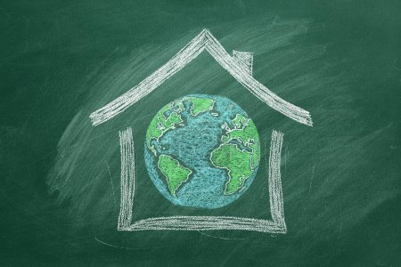 Foto de Un dibujo de tiza de la Tierra está encerrado dentro de un contorno de la casa en una pizarra de aula verde, que simboliza la unidad global. La Tierra es nuestro hogar. - Imagen libre de derechos