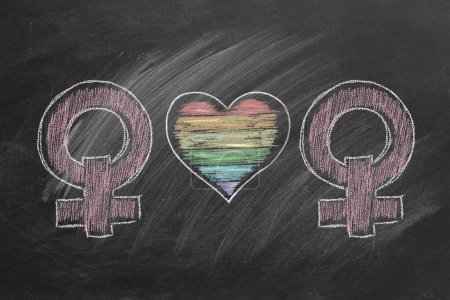 Foto de Two female gender symbols with a colorful rainbow heart, drawn in vibrant chalk on a dark chalkboard, symbolizing love, pride, and equality. - Imagen libre de derechos