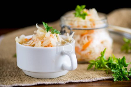 Sauerkraut with carrots and spices in a bowl on a wooden table.