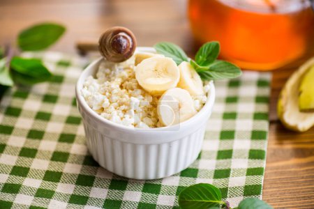 Téléchargez les photos : Fromage cottage bio friable avec du miel et des bananes dans un bol en céramique sur la table - en image libre de droit