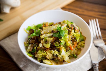 cabbage early fried with mushrooms, carrots and vegetables in a white bowl on a wooden table