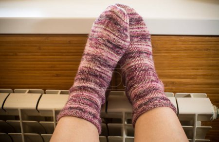 Téléchargez les photos : Pieds dans des chaussettes d'hiver chaudes réchauffer sur le radiateur par temps froid d'hiver. - en image libre de droit