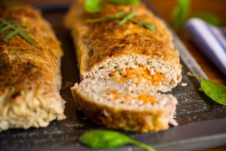 Cooked minced meatloaf with vegetable filling inside, on a wooden table.