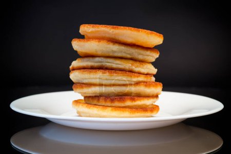gekochte süße Pfannkuchen mit Honig in einem Teller isoliert auf schwarzem Hintergrund