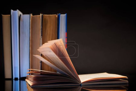 Téléchargez les photos : Livre ouvert pour la lecture et une pile de livres, isolé sur un fond noir. - en image libre de droit