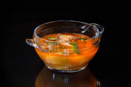 Téléchargez les photos : Soupe de tomates de légumes avec du poisson dans une assiette isolée sur fond noir - en image libre de droit