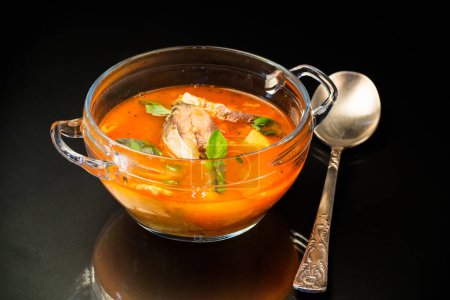 Téléchargez les photos : Soupe de tomates de légumes avec du poisson dans une assiette isolée sur fond noir - en image libre de droit