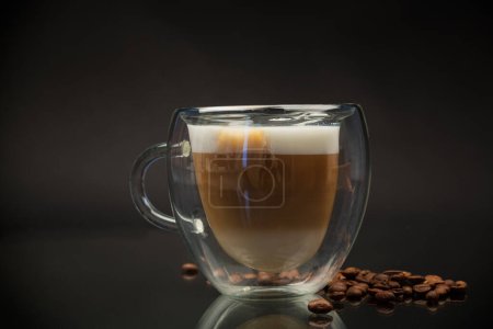 Téléchargez les photos : Café chaud avec du lait dans une tasse en verre isolé sur fond noir - en image libre de droit