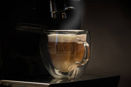 Téléchargez les photos : Café chaud avec du lait dans une tasse en verre isolé sur fond noir - en image libre de droit