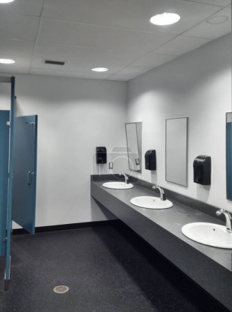 Photo for Simple but clean public washroom, row of sinks, mirrors and toilet stalls, grungy faded-color mobile shot - Royalty Free Image