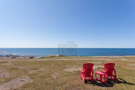 Photo for Red Adirondack Chairs overlooking barren coastal landscape of Newfoundland, NL, Canada - Royalty Free Image