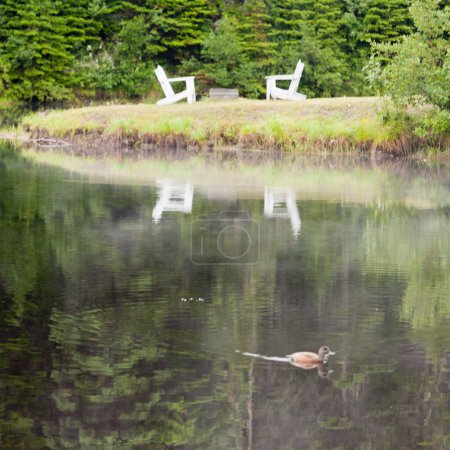Téléchargez les photos : Deux chaises adirondacks en bois face au lac avec réflexion sur la surface de l'eau - en image libre de droit