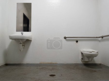 Einfache öffentliche Barebone-Toilette mit Spiegel und Waschbecken sowie WC-Schüssel über Betonboden mit Abfluss für eine einfache Reinigung