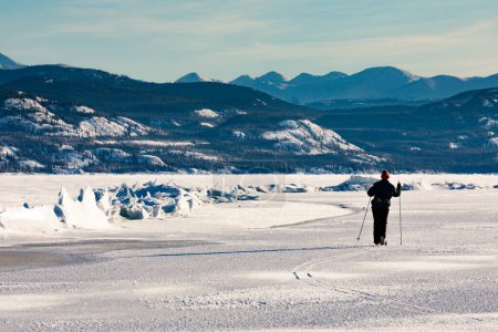 Cross-country skier exploring pressure ridge caused by tension stress between ice floes in frozen winter wonderland landscape of  Lake Laberge, Yukon Territory, Canada