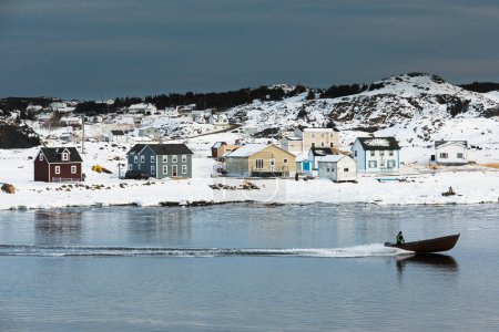 Photo for Motor boat enters Durrell Harbour of outport town of Twillingate passing traditional wooden saltbox residential houses in winter, Newfoundland, NL, Canada - Royalty Free Image