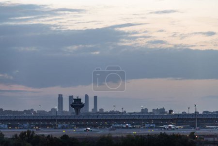 Panorama view of the T4 terminal of Madrid Barajas airport at dusk, with the skyline of the city and its four skyscrapers in the background.