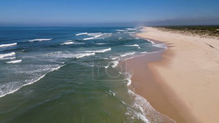 Side view of waves crashing on sandy beach aerial - a bird's eye view of ocean waves crashing against an empty beach from above.