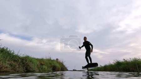 Tragflügelfahrer gleitet an einem bewölkten Tag mit seinem Board über das Wasser in einem der Kanäle der Ria de Aveiro in Portugal.