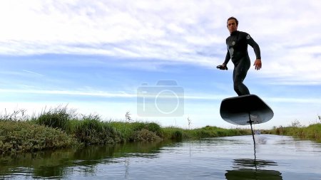Hydrofoil rider gliding over the water with his board in one of the canals of the Ria de Aveiro in Portugal on a cloudy day.