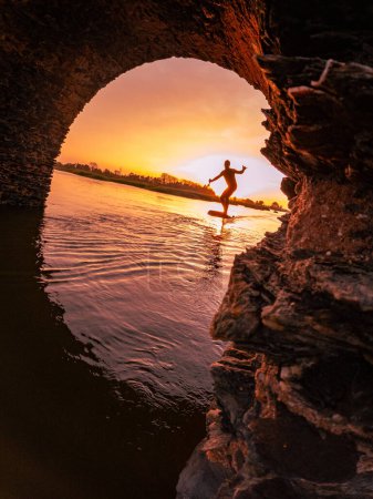 Tragflügelfahrer gleitet bei Sonnenuntergang mit seinem Board über das Wasser in einem der Kanäle der Ria de Aveiro in Portugal.