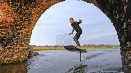 Hydrofoil rider gliding over the water with his board in one of the canals of the Ria de Aveiro in Portugal during sunset.