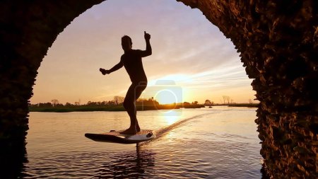 Hydrofoil rider gliding over the water with his board in one of the canals of the Ria de Aveiro in Portugal during sunset.