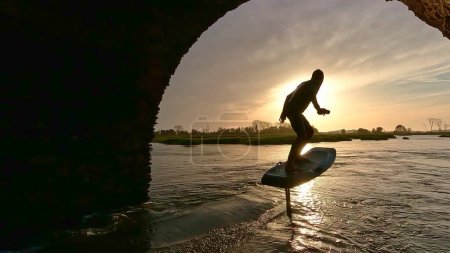 Tragflügelfahrer gleitet bei Sonnenuntergang mit seinem Board über das Wasser in einem der Kanäle der Ria de Aveiro in Portugal.