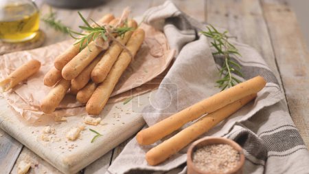 Traditional italian breadsticks grissini with rosemary, olive oil and sesame seeds on wooden countertop.