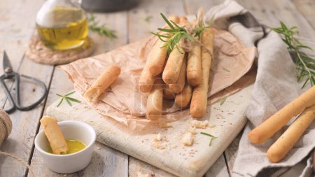 Traditional italian breadsticks grissini with rosemary, olive oil and sesame seeds on wooden countertop.
