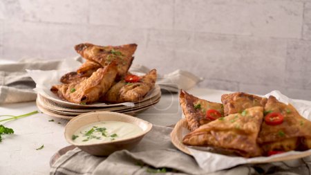 Indische Samosas - gebackenes oder gebackenes Gebäck mit pikanter Füllung, beliebte indische Snacks, serviert in areca-Blättergerichten mit Gewürzen auf der Arbeitsplatte.