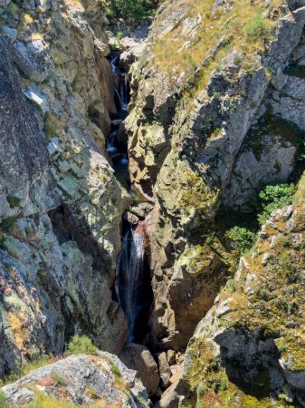 An aerial view of a narrow gorge with a cascading waterfall surrounded by rugged rocks. Guarda, Portugal.