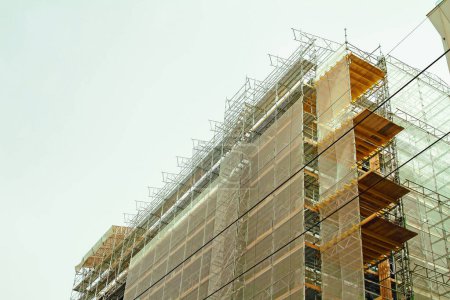 Baugerüste mit Staubschutzhülle und Gerüste bieten Plattformen Baustelle des modernen Gebäudes. Arbeiten an einem neuen Wohnblock.