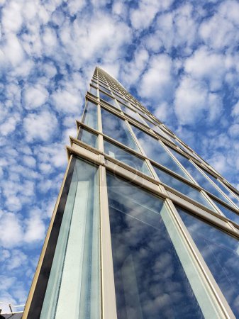 Foto de Vista de abajo hacia arriba de un edificio de oficinas moderno contra un cielo azul con nubes blancas clima soleado. Estilo azul y blanco - Imagen libre de derechos
