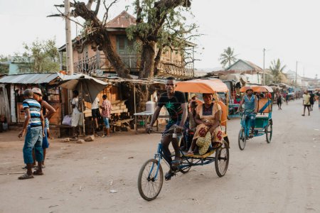 Foto de Miandrivazo, Madagascar - November 1. 2022: Traditional rickshaw bicycle with Malagasy passengers on the street, one of the ways to earn money. Everyday life on the cities street of Madagascar. - Imagen libre de derechos
