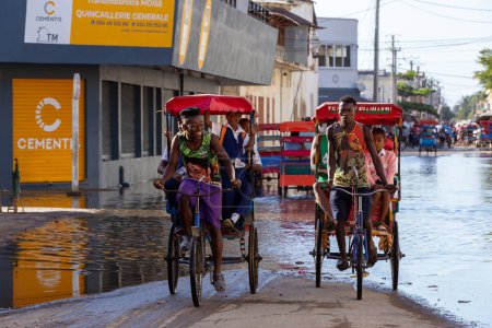 Foto de Toliara, Madagascar - 21 de noviembre. 2022: Tradicional bicicleta rickshaw con pasajeros malgaches en la calle, una de las maneras de ganar dinero. La vida cotidiana en las ciudades calle de Madagascar. - Imagen libre de derechos