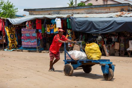 Foto de Miandrivazo, Madagascar - 2 de noviembre de 2022: Un hombre involucrado en el transporte de bolsas empuja un carro primitivo en las calles de Miandrivazo. - Imagen libre de derechos