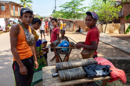 Foto de Miandrivazo, Madagascar - 2 de noviembre de 2022: Vendedores ambulantes que venden "koba", un dulce tradicional malgache hecho de cacahuetes molidos, azúcar morena y harina de arroz, que refleja el patrimonio culinario local. - Imagen libre de derechos