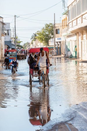 Foto de Toliara, Madagascar - 21 de noviembre. 2022: Tradicional bicicleta rickshaw con pasajeros malgaches en la calle, una de las maneras de ganar dinero. La vida cotidiana en las ciudades calle de Madagascar. - Imagen libre de derechos