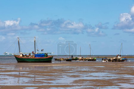 Foto de Toliara, Madagascar - 21 de noviembre de 2022: Barco de pesca varado en el puerto seco durante la marea baja con gente malgache alrededor. - Imagen libre de derechos