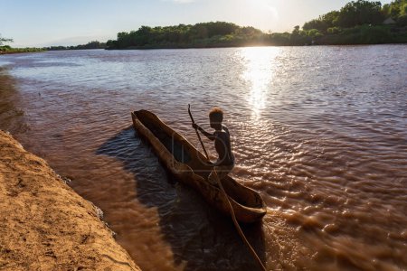 Téléchargez les photos : Silhouette d'un Ferryman pagayant sur un bateau traditionnel en bois grossier, traversant la rivière Omo, vallée de l'Omo, Omorati Etiopia - en image libre de droit