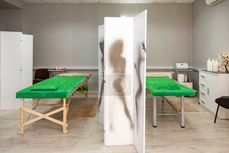 Helle, moderne Details im Massageraum, zwei grüne Massageliegen mit beigen Decken, Trennwand mit Bild der Silhouette der Frau