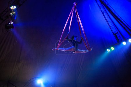 Correas aéreas profesionales seda mujer gimnasta circo rendimiento en la arena roja con fondo oscuro retroiluminado con luces de concierto de colores, la realización de elemento gimnástico