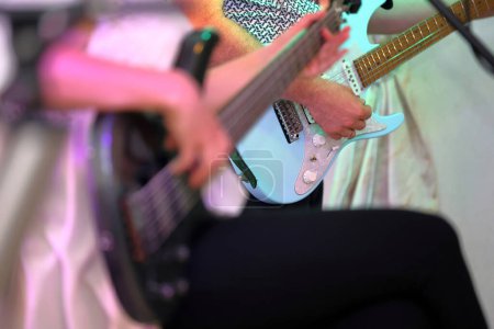 Photo for Closeup of a man's hand playing an electric guitar at a concert, in the background a woman playing a bass guitar, and an empty space for text. - Royalty Free Image