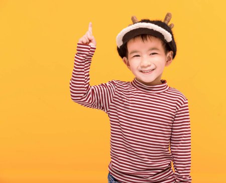 Téléchargez les photos : Enfant heureux habillé en chapeau de Noël et pointant vers le haut - en image libre de droit